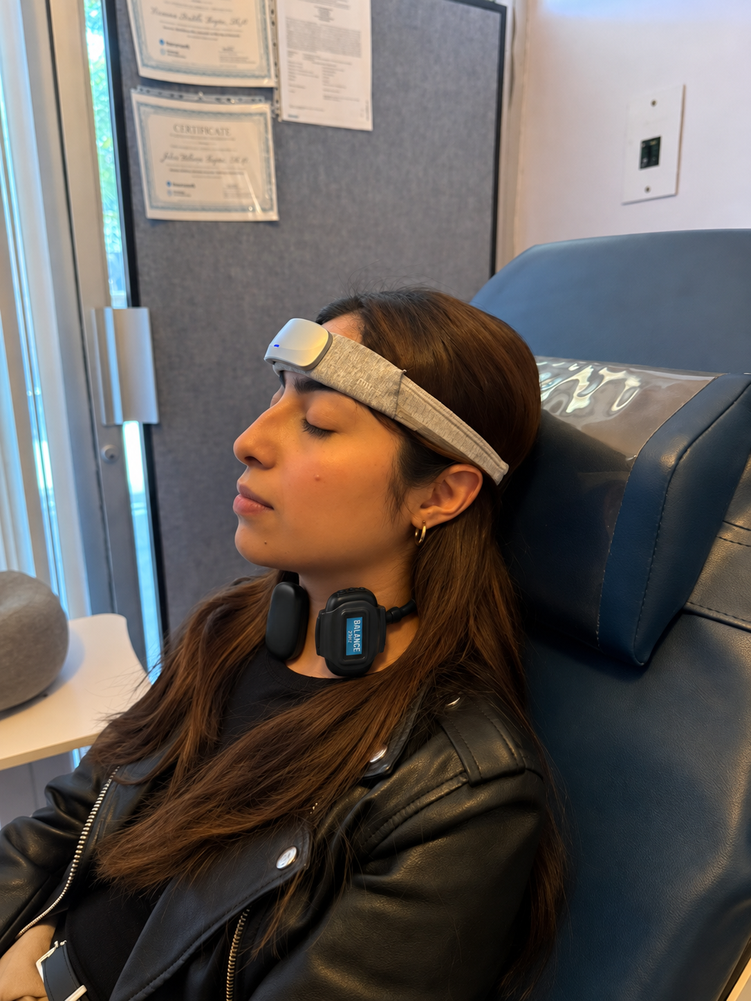 Persona recostada en silla azul de NeuroSpa con dispositivo externo de estimulación eléctrica colocado en el cuello y banda de neuroterapia en la frente.